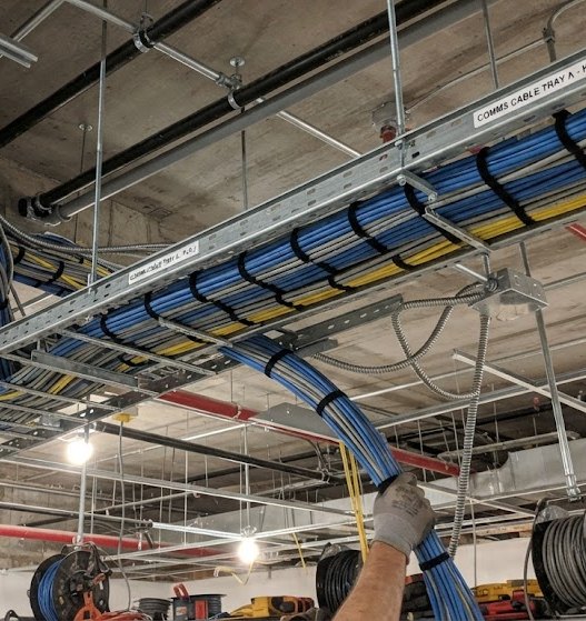 Structured cabling pulled along galvanised cable tray in an open ceiling void, bundled and tied at intervals